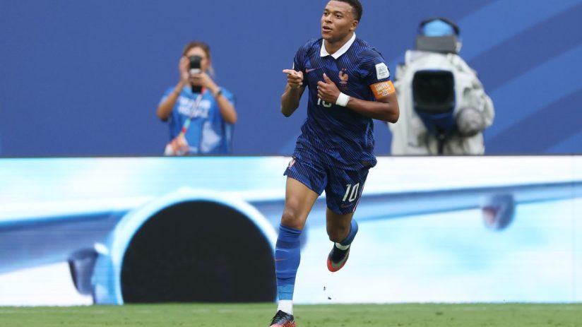 Kylian Mbapp&eacute; in a blue France soccer jersey with number 10, celebrating a goal on a green field.