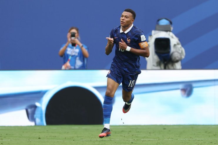Kylian Mbapp&eacute; in a blue France soccer jersey with number 10, celebrating a goal on a green field.