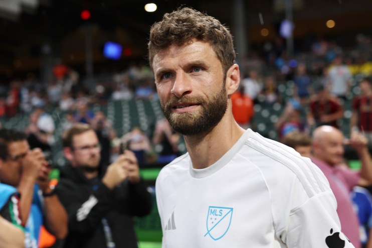 Thomas M&uuml;ller in a white MLS jersey looking forward with fans in the background at a stadium event.