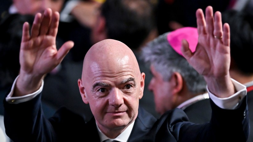 Gianni Infantino, FIFA President, raising both hands, wearing a suit with a World Cup pin.