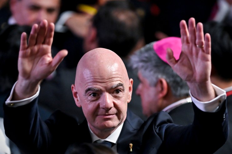 Gianni Infantino, FIFA President, raising both hands, wearing a suit with a World Cup pin.