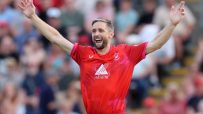 Chris Woakes, cricketer in a red uniform, raising his arms in celebration on the field.