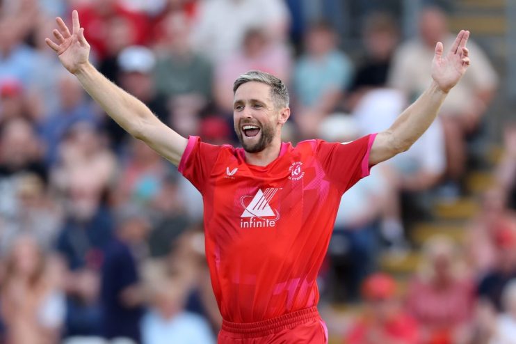 Chris Woakes, cricketer in a red uniform, raising his arms in celebration on the field.