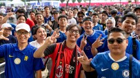 Enthusiastic football fans, some in Chelsea and AC Milan jerseys, smiling and making peace signs at an event.
