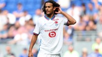 A male soccer player with long dark curly hair in a white LOSC Lille jersey adjusts his hair on the field.