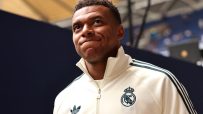 Kylian Mbapp&eacute; in a cream-colored Adidas track jacket with the Real Madrid crest, looking up with a thoughtful expression