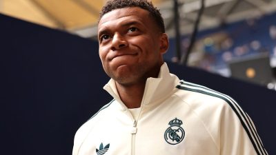 Kylian Mbapp&eacute; in a cream-colored Adidas track jacket with the Real Madrid crest, looking up with a thoughtful expression