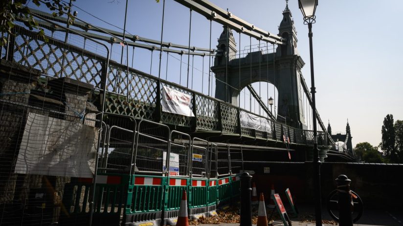 Hammersmith Bridge closed in 2021 with fencing, banners, and traffic cones blocking access to the walkway.