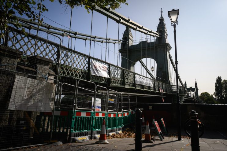 Hammersmith Bridge closed in 2021 with fencing, banners, and traffic cones blocking access to the walkway.