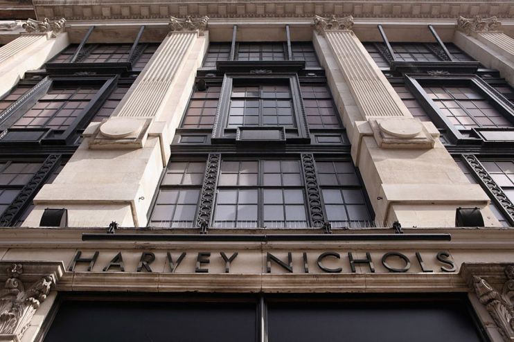 Low-angle view of the Harvey Nichols store facade with large windows, ornate columns, and prominent signage.