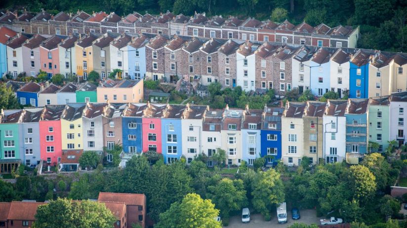 Aerial view of colorful residential houses built on a hillside, nestled among green trees, representing housing markets