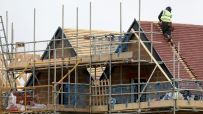 Construction worker on a new house roof, surrounded by scaffolding and building materials, illustrating housebuilding.