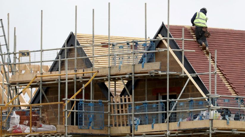 Construction worker on a new house roof, surrounded by scaffolding and building materials, illustrating housebuilding.