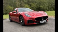 Red Maserati sports car parked on asphalt with trees and grass in the background.