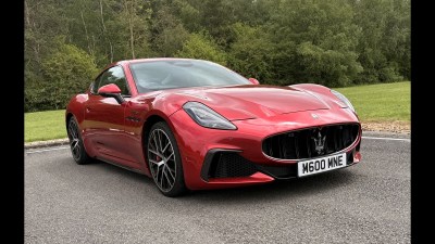 Red Maserati sports car parked on asphalt with trees and grass in the background.