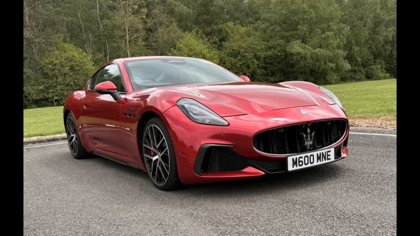 Red Maserati sports car parked on asphalt with trees and grass in the background.