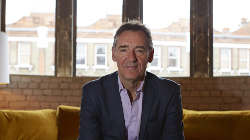 Jim ONeill, economist and former Goldman Sachs chairman, sitting on a yellow sofa in front of large windows.