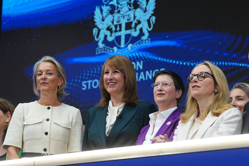 Julia Hoggett and Rachel Reeves smiling at a business event, with a screen displaying a crest in the background