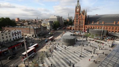 Aerial view of Kings Cross St. Pancras station and square, London, with people, buses, and surrounding buildings.