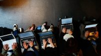 Overhead view of several laptop workers typing on computers, seated on a dark floor.