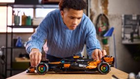 Young man in a blue sweater assembling a black and orange Lego McLaren Formula 1 race car model