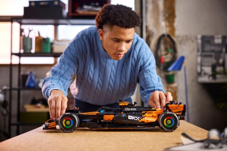 Young man in a blue sweater assembling a black and orange Lego McLaren Formula 1 race car model