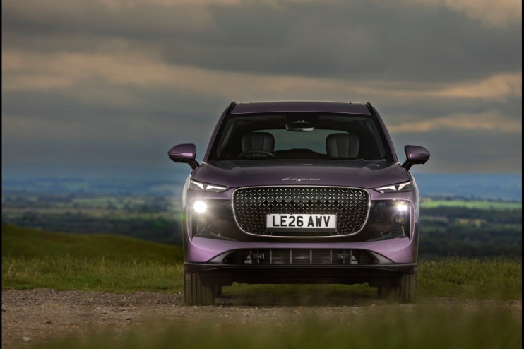 Front view of a purple SUV, possibly a Lepas L8, with headlights on, on a dirt road against a cloudy sky.