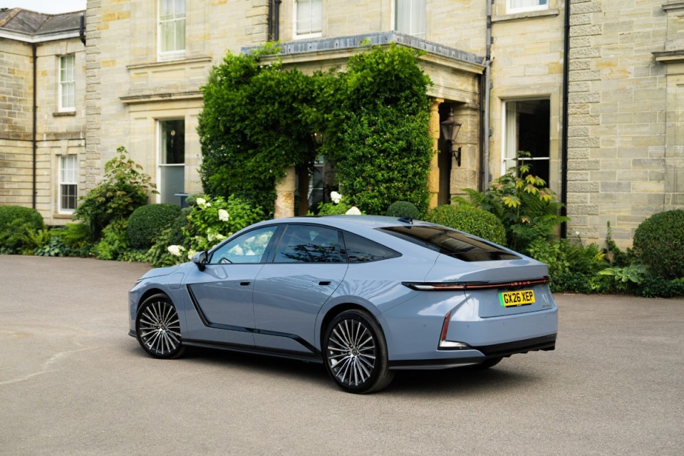 Light blue Lexus ES350e parked on a driveway in front of a large stone building with green foliage.