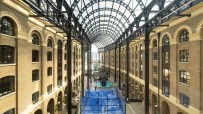 Overhead view of a blue padel court and people playing inside Londons Hays Galleria, under a glass and steel roof.