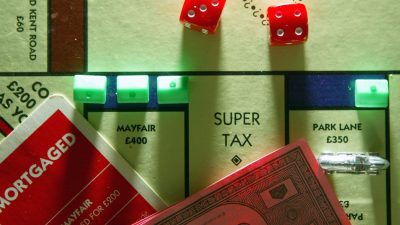 Monopoly board game with Super Tax space, red dice, and property cards, representing taxation concepts.