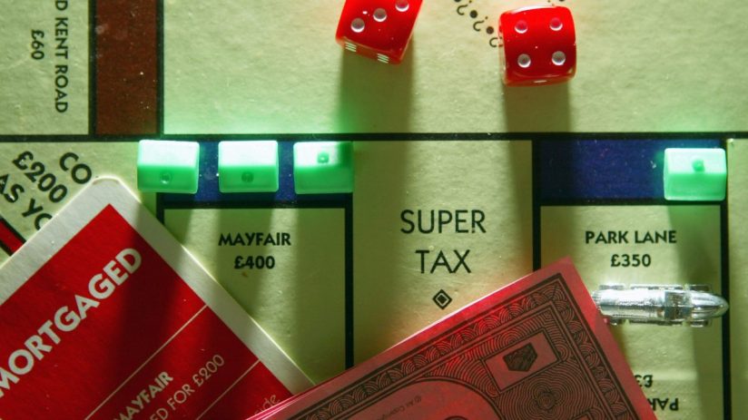Monopoly board game with Super Tax space, red dice, and property cards, representing taxation concepts.