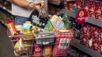 Shopper holding a basket filled with Morrisons groceries, including tortilla chips, bread, and flour, next to an Unbeatabl...