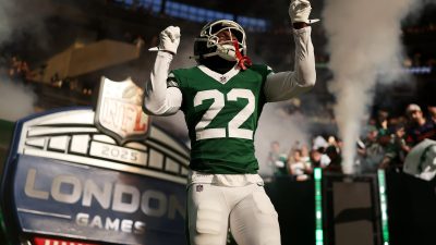 NFL player in green #22 jersey with arms raised, emerging through smoke onto the field at NFL London Games.