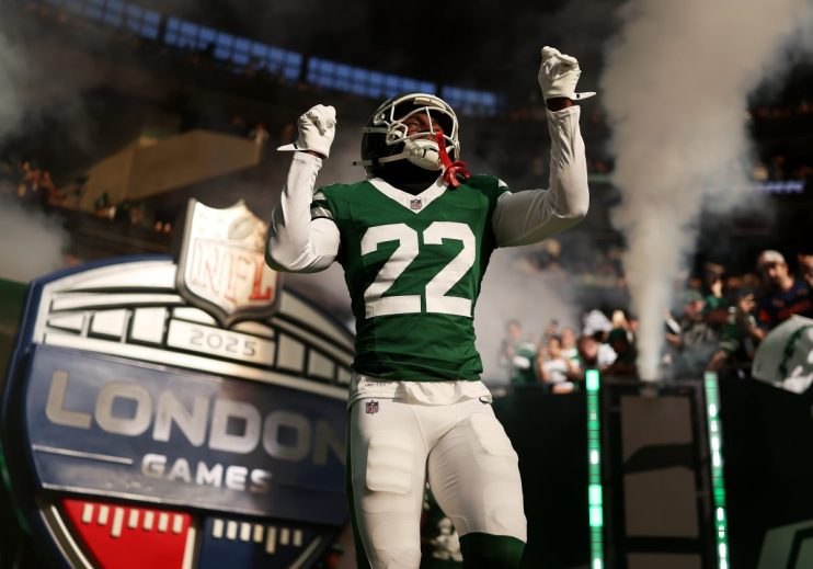 NFL player in green #22 jersey with arms raised, emerging through smoke onto the field at NFL London Games.