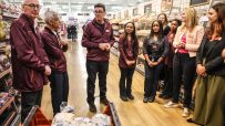 Andy Burnham, Sadiq Khan, and Sainsburys staff discussing Neets numbers in a supermarket bakery aisle.