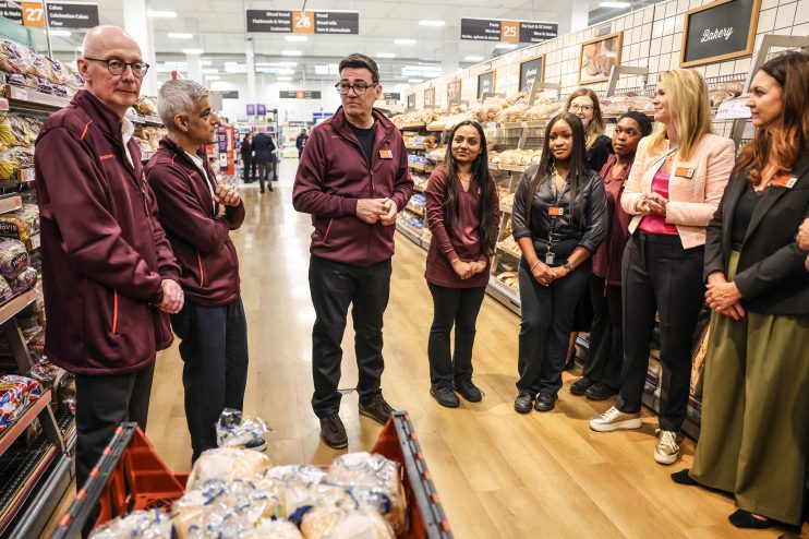 Andy Burnham, Sadiq Khan, and Sainsburys staff discussing Neets numbers in a supermarket bakery aisle.