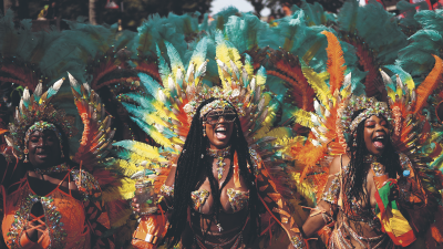 Three revelers in vibrant feathered costumes celebrating at Notting Hill Carnival.