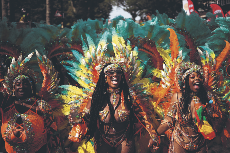 Three revelers in vibrant feathered costumes celebrating at Notting Hill Carnival.