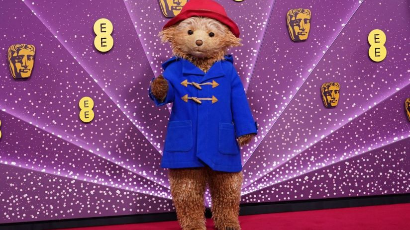 Paddington Bear in a blue duffle coat and red hat on a purple background with BAFTA and EE logos