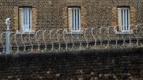 Brick prison wall with barred windows, razor wire, and a security camera.