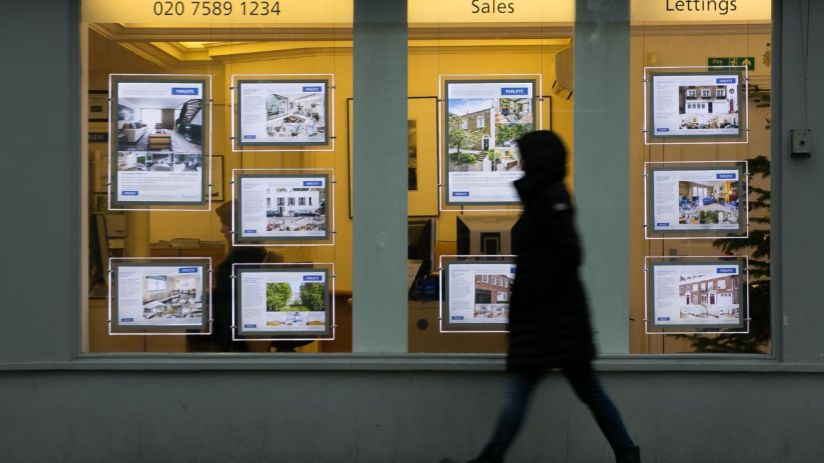 Person walks past a real estate agents window displaying properties for sale and to let.