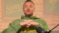 Man in a green hoodie speaking into a microphone, with a 5000 sign in the background.