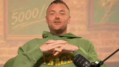 Man in a green hoodie speaking into a microphone, with a 5000 sign in the background.