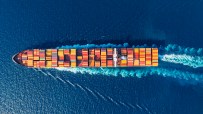 Aerial view of a large container ship moving through deep blue ocean waters, leaving a white wake.