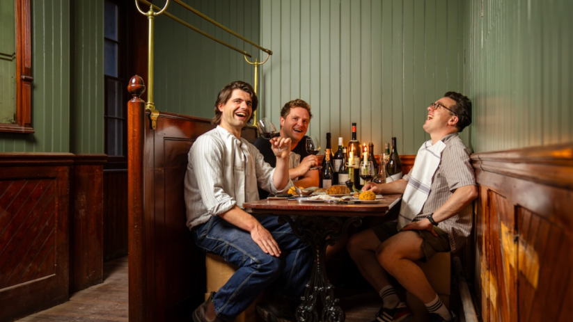 Three men enjoying wine and food, laughing in a cozy booth at Simpsons Tavern Cloth, Cornhill