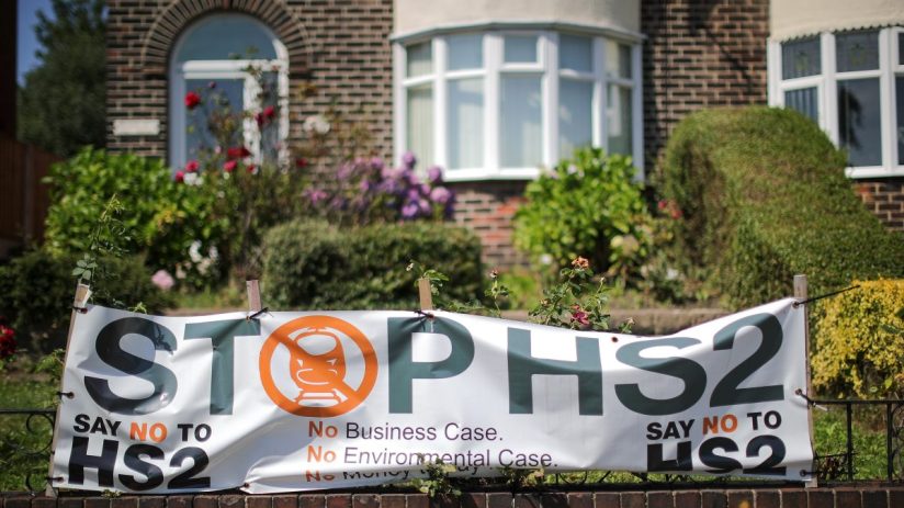 Stop HS2 banner with a train icon, displayed on a brick wall in front of a house, protesting the HS2 project