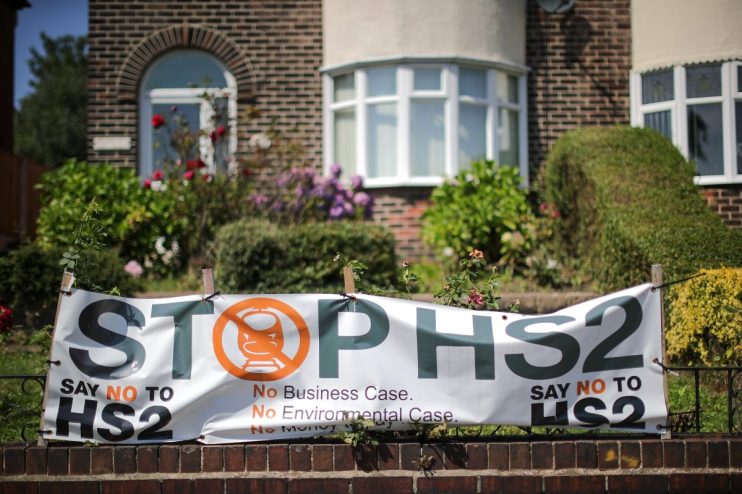 Stop HS2 banner with a train icon, displayed on a brick wall in front of a house, protesting the HS2 project