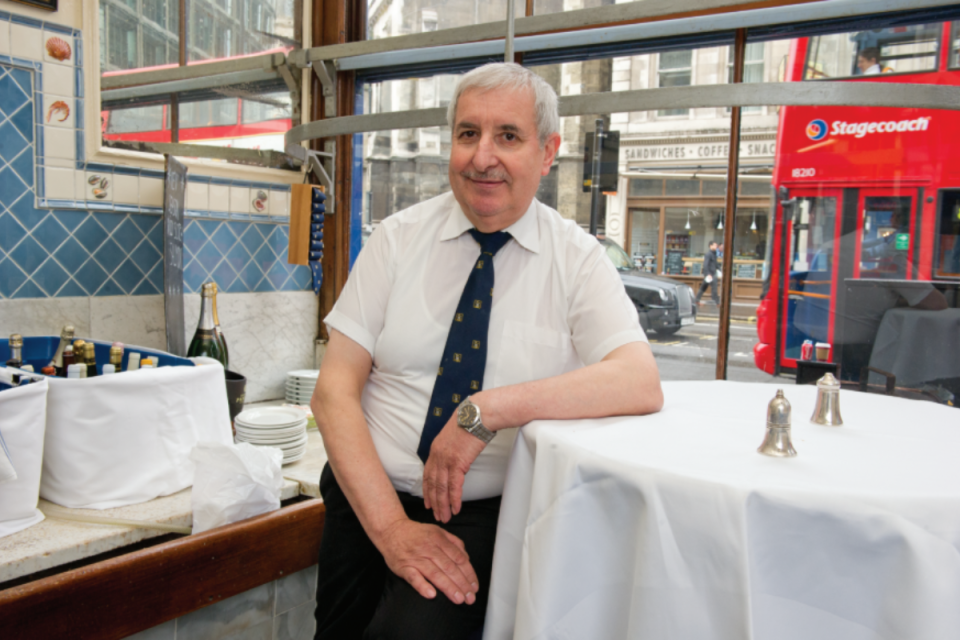 Sweetings City of London staff member with a red double-decker bus passing by outside.