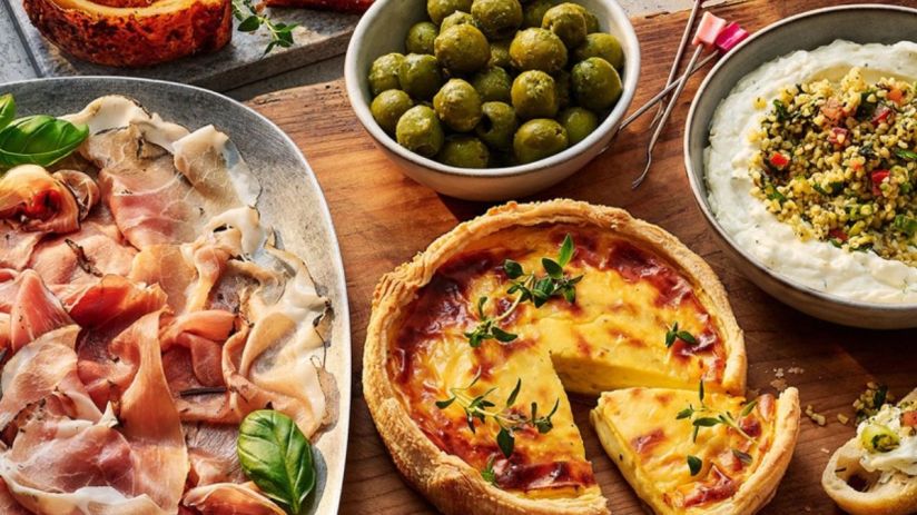 Tesco quiche, cured meats, olives, and dip on a wooden board, ready for a party or meal.