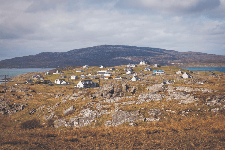 Coastal village with white houses on a rocky, grassy hillside in the Outer Hebrides under a cloudy sky